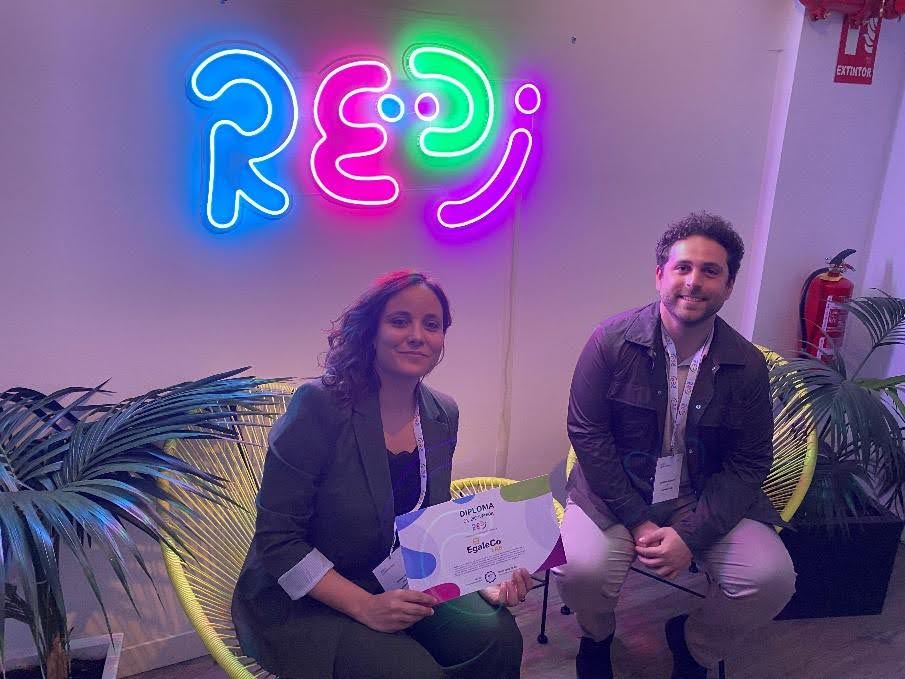Silvia Soto y José Luis Izaguirre, representantes de EgaleCo Lab, posan con el diploma de adhesión a REDI frente al logotipo iluminado de la red, durante el evento celebrado en Madrid en noviembre de 2024.