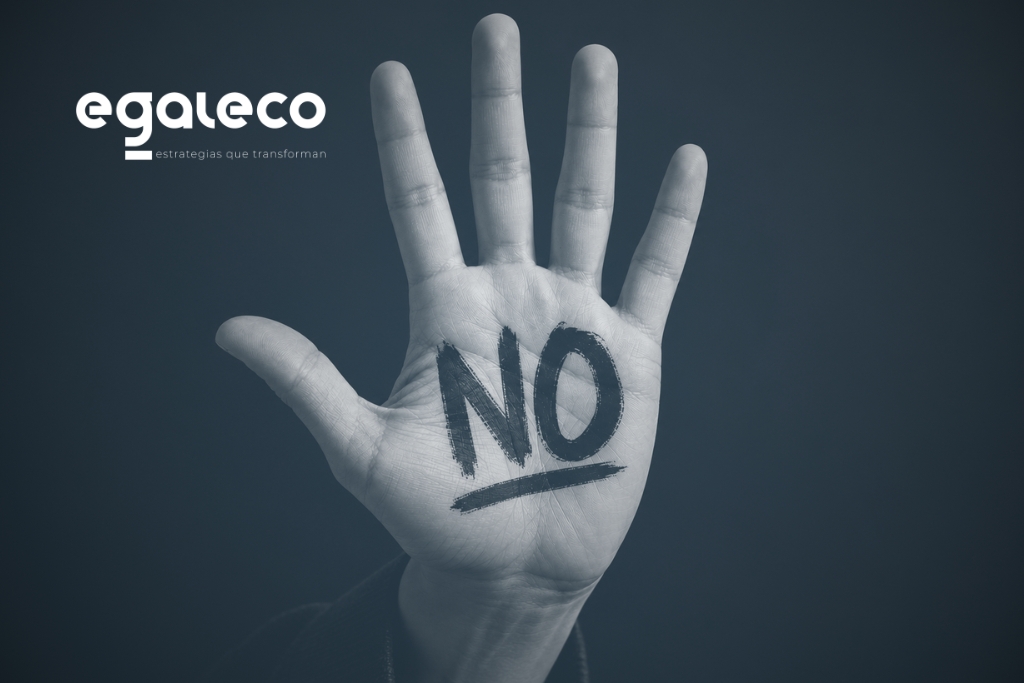 Mano levantada con la palabra “NO” sobre fondo negro, como símbolo de prevención frente al acoso sexual y por razón de sexo.